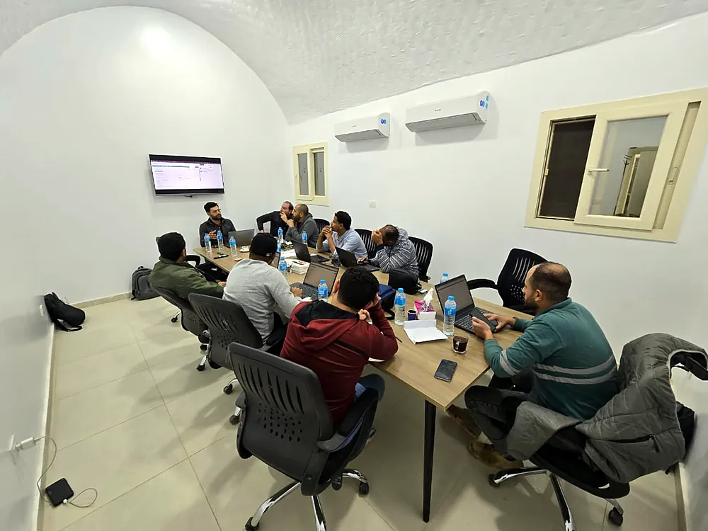 The IBS team in a working session around a meeting table, with a system screen on the wall